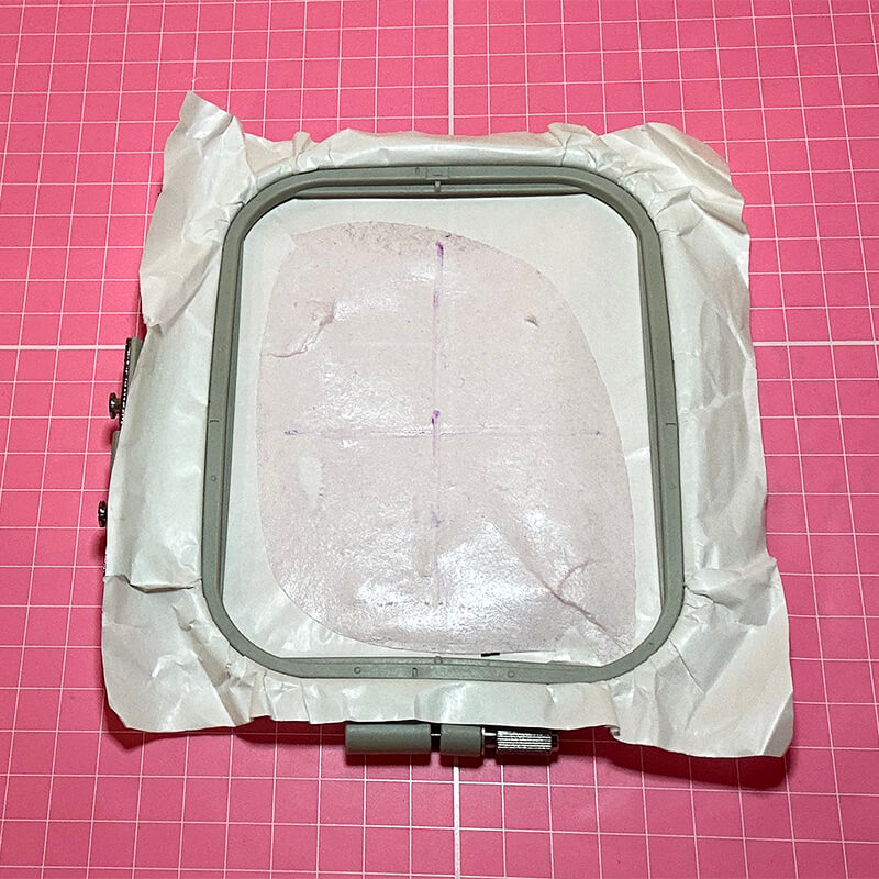 Prepare your embroidery hoop
Hoop a piece of sticky back stabilizer. Score around the inside edge of the hoop with a pin and peel away the top paper.  Draw horizontal and vertical lines through the center of the hoop on the exposed sticky stabilizer.